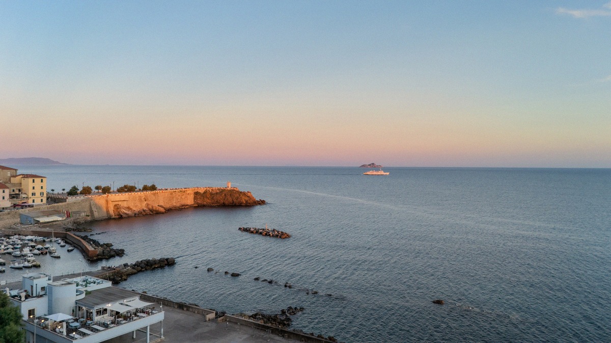 Abendstimmung über Piombino mit Leuchtturm und Festungsmauer, auf dem Meer eine Fähre